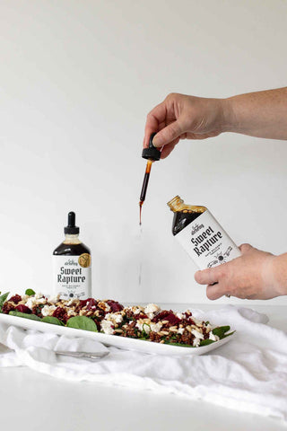 Hands drizzling Lady Alchemy Sweet Rapture Date Balsamic Treacle over a fresh salad with spinach, beetroot, feta and pine nuts — clean artisan condiments made in New Zealand