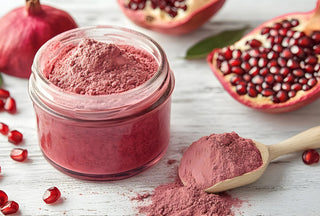 Jar of pink powder with pomegranate seeds and a wooden spoon on a light surface