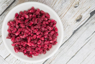 Frozen red berries in a white ceramic bowl, photographed from above on a rustic white wooden surface.